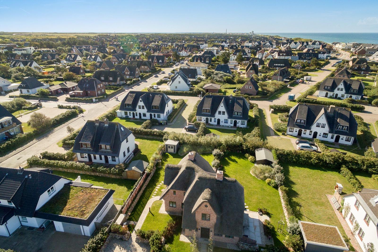 Aerial view of a coastal village with traditional houses and green lawns.