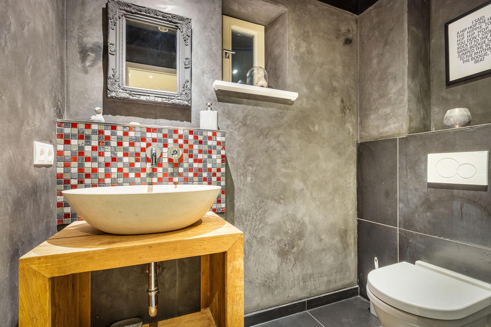 Bathroom with sink on wooden stand, mosaic wall, and toilet.