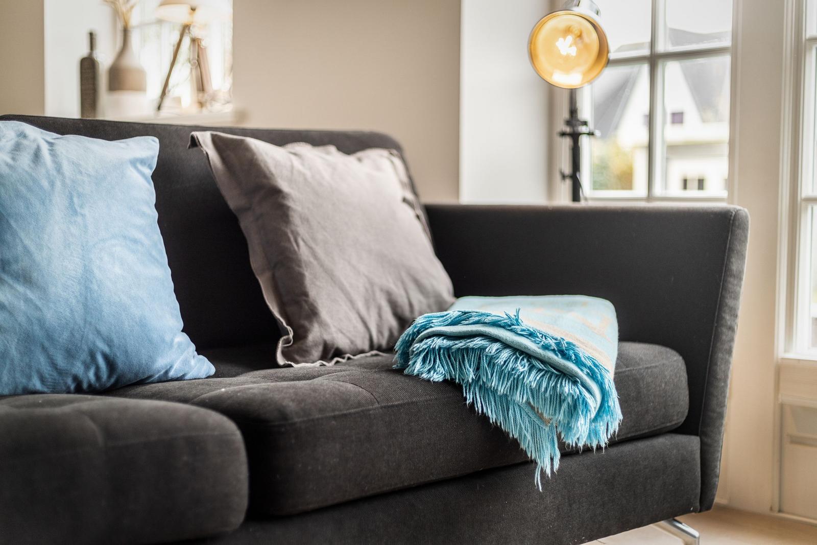 A dark sofa with blue cushions and a blanket.