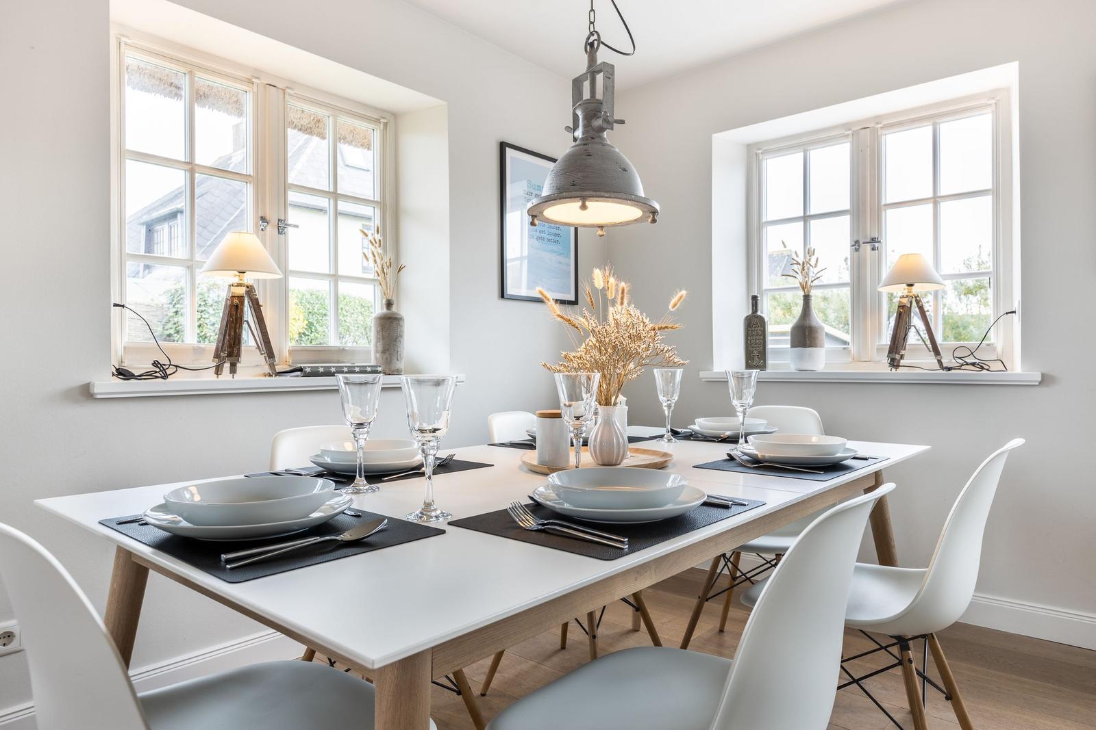 Dining room with table, chairs, and windows. Table set with dishes and glasses.