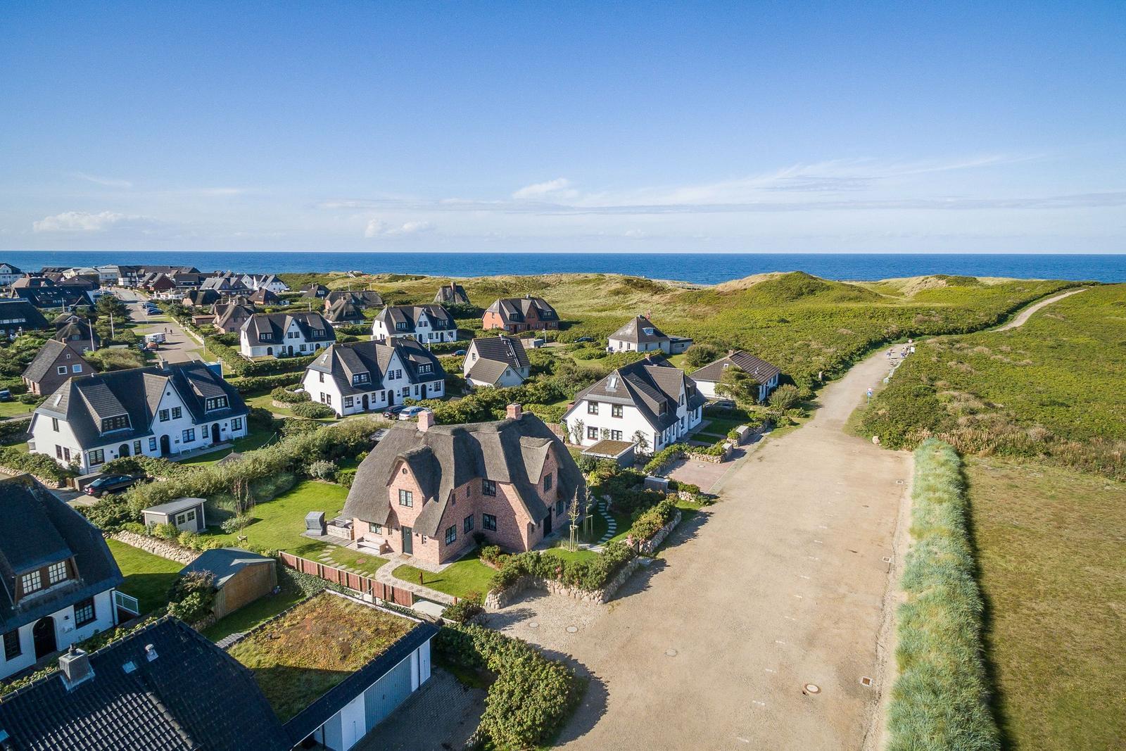 Houses by the sea with green areas and sandy path.