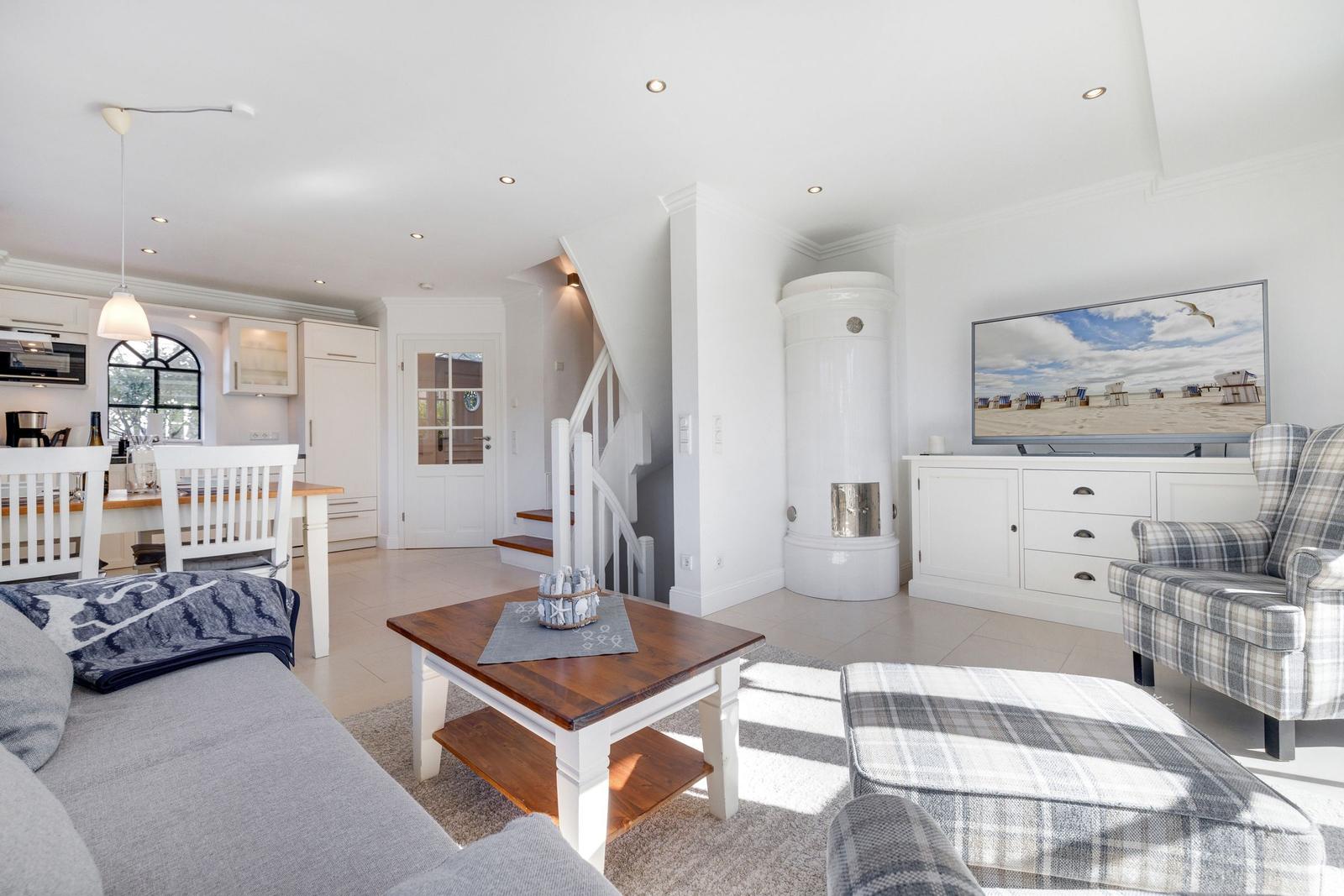 Wohnzimmer mit Sofa, Sessel und Kamin. Küche und Treppe sind sichtbar.
