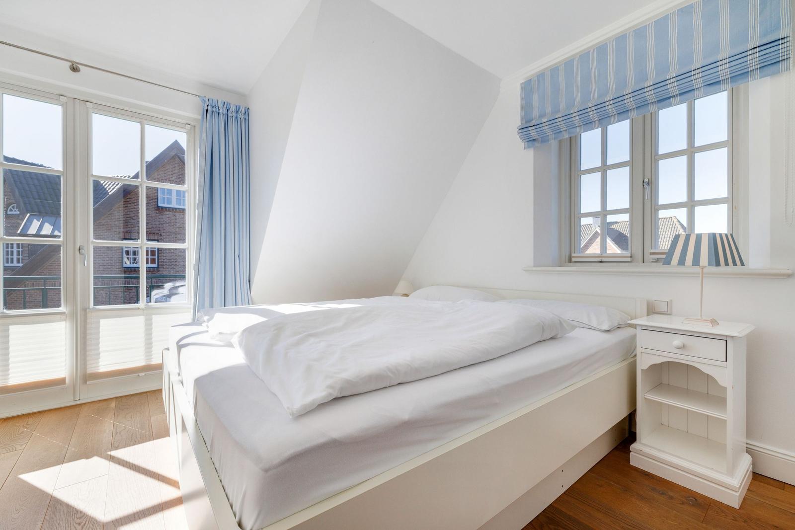 Schlafzimmer mit Doppelbett, Fenster und Holzboden.