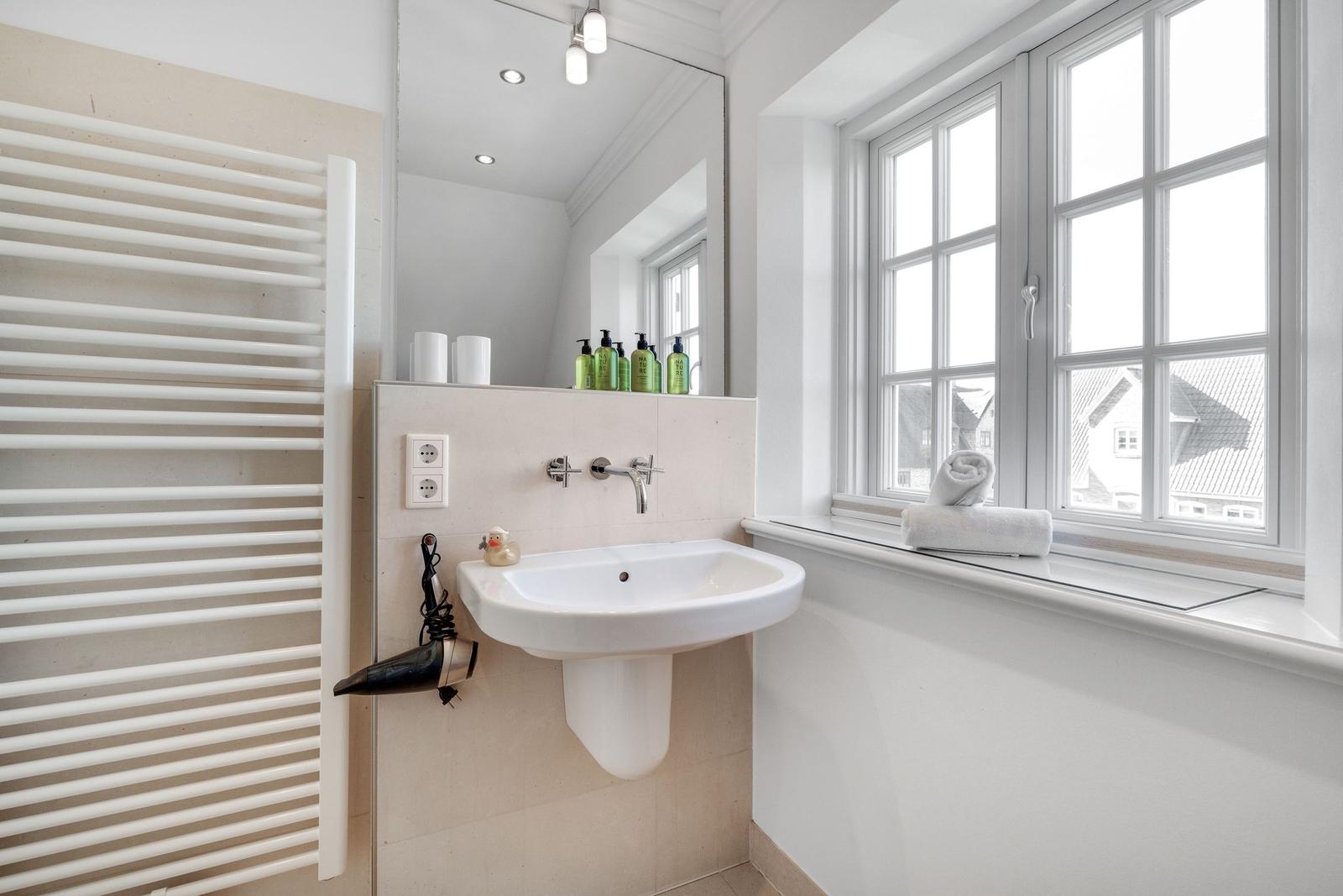 Badezimmer mit Waschbecken, Spiegel und Fenster. Handtuch und Duschgel sind vorhanden.