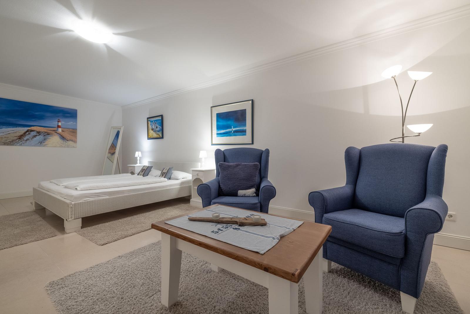 Schlafzimmer mit Bett, zwei blauen Sesseln und Wandbildern.
