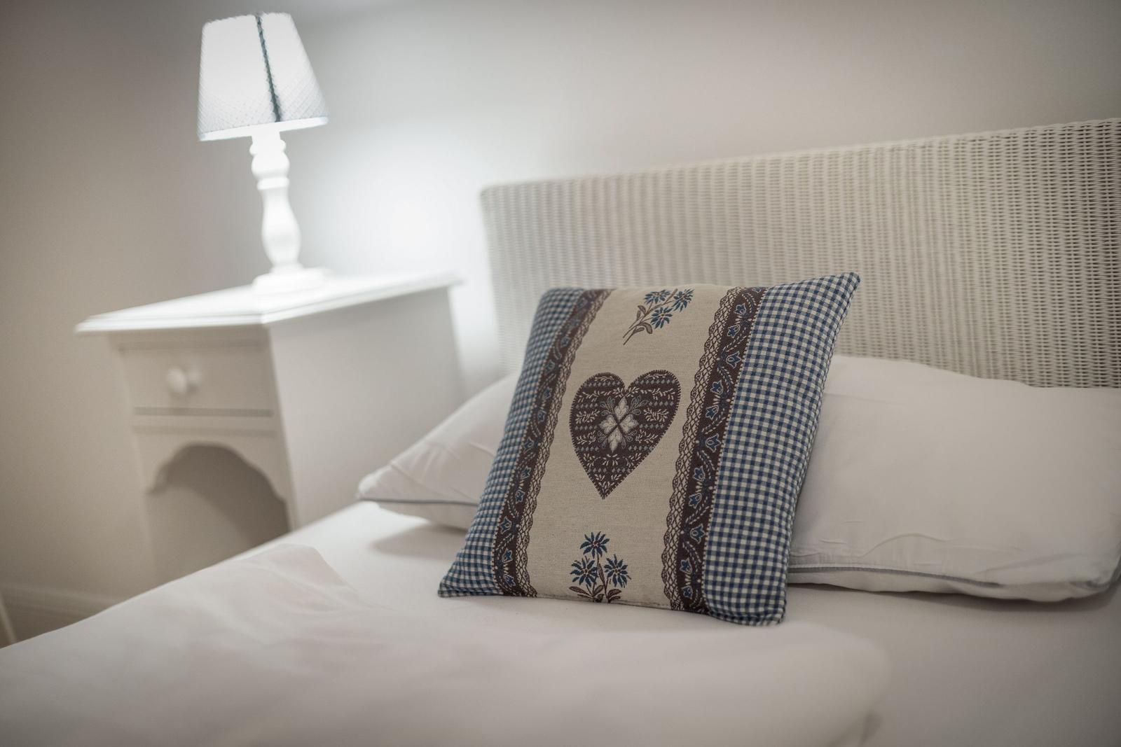 Bettkopfteil aus geflochtenem Material, Kissen mit Herz und Blumenmuster, Nachttisch mit Lampe.