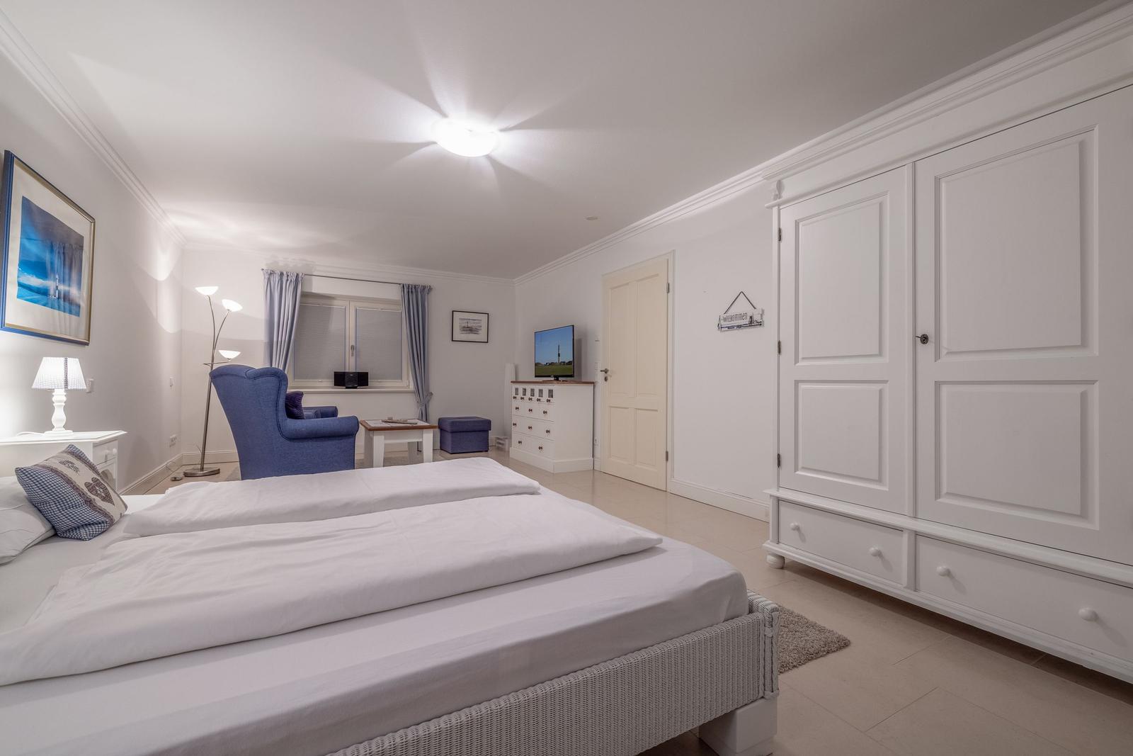 Schlafzimmer mit Bett, Kleiderschrank und Sitzgelegenheit.