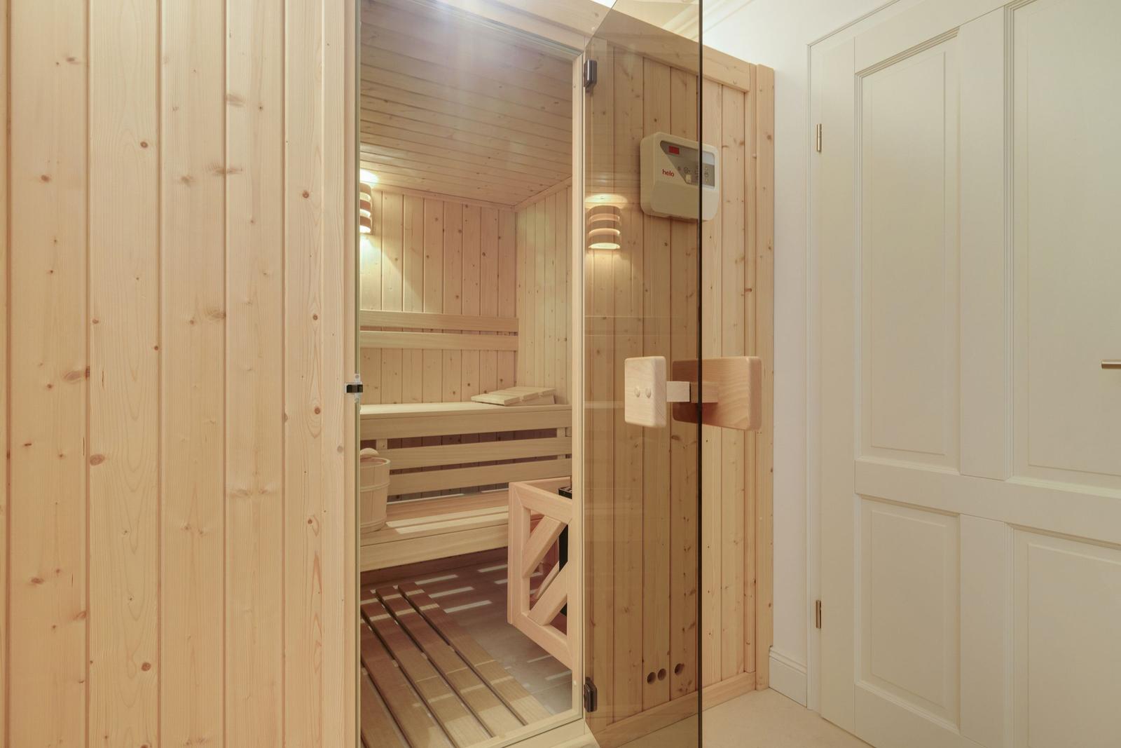 Sauna mit Holzverkleidung und Glasfront. Innere Bänke und Heizgerät sichtbar.