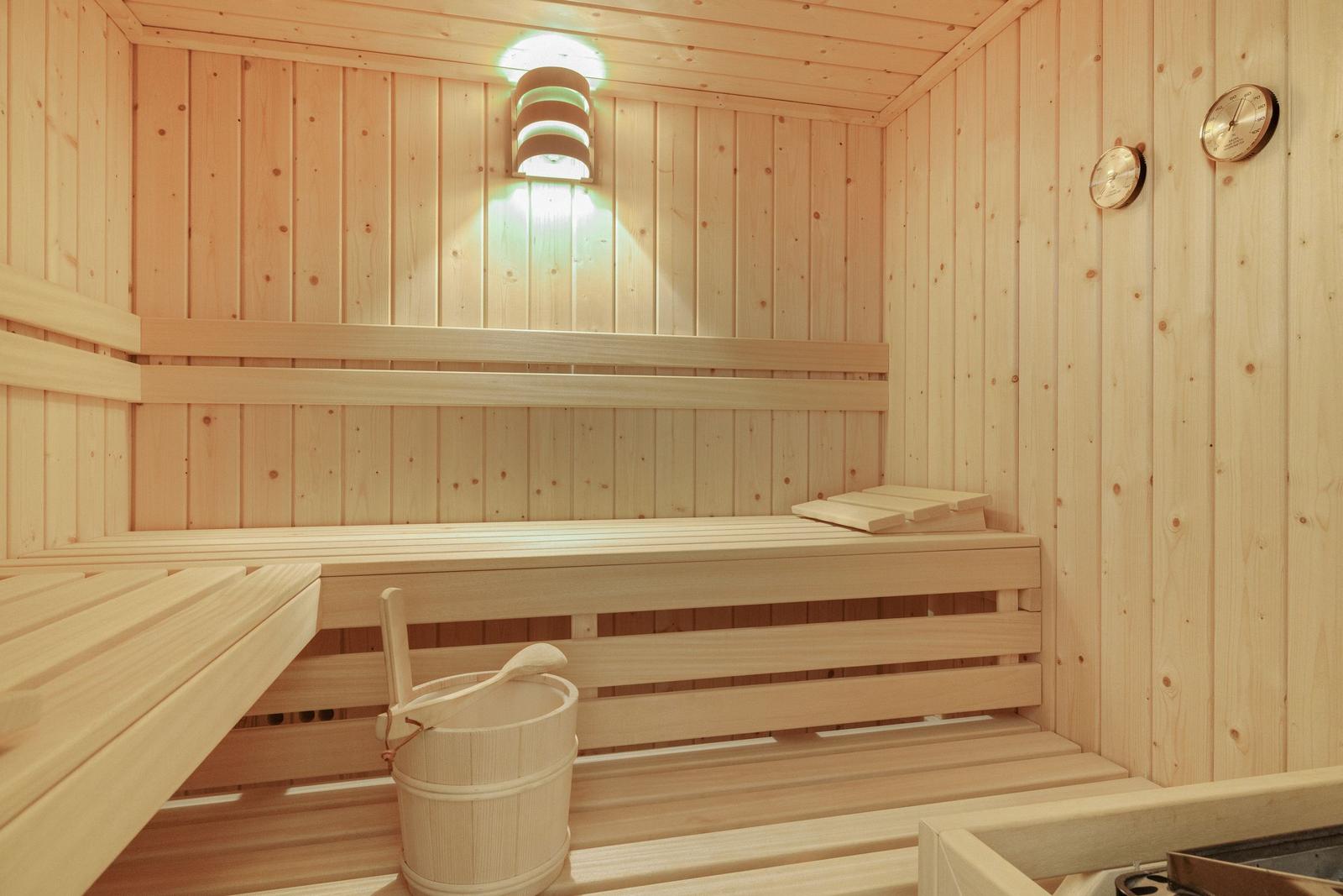 Holzsauna mit Sitzbänken, Eimer und Thermometer an den Wänden.