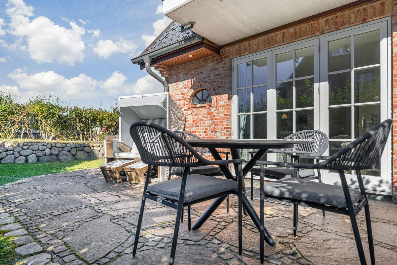 Terrasse mit Tisch und Stühlen vor einem Haus mit Backsteinwand und Fenstern.