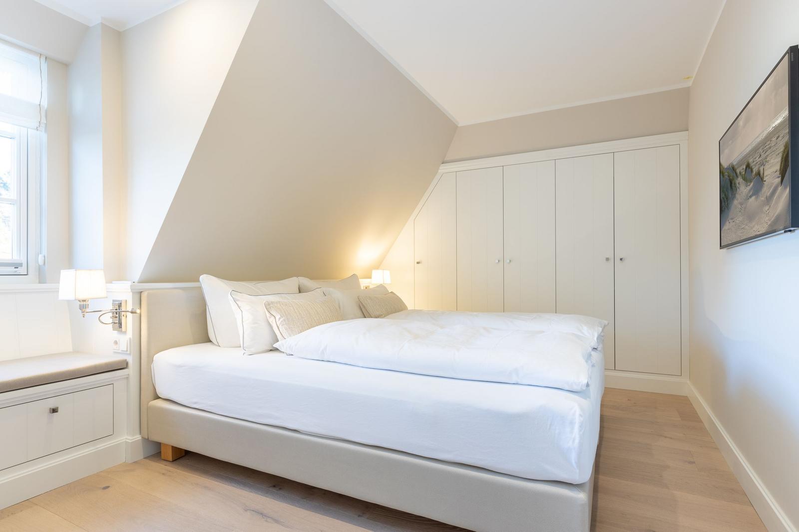 Schlafzimmer mit Dachschräge, Bett, Kleiderschrank und Fenster.