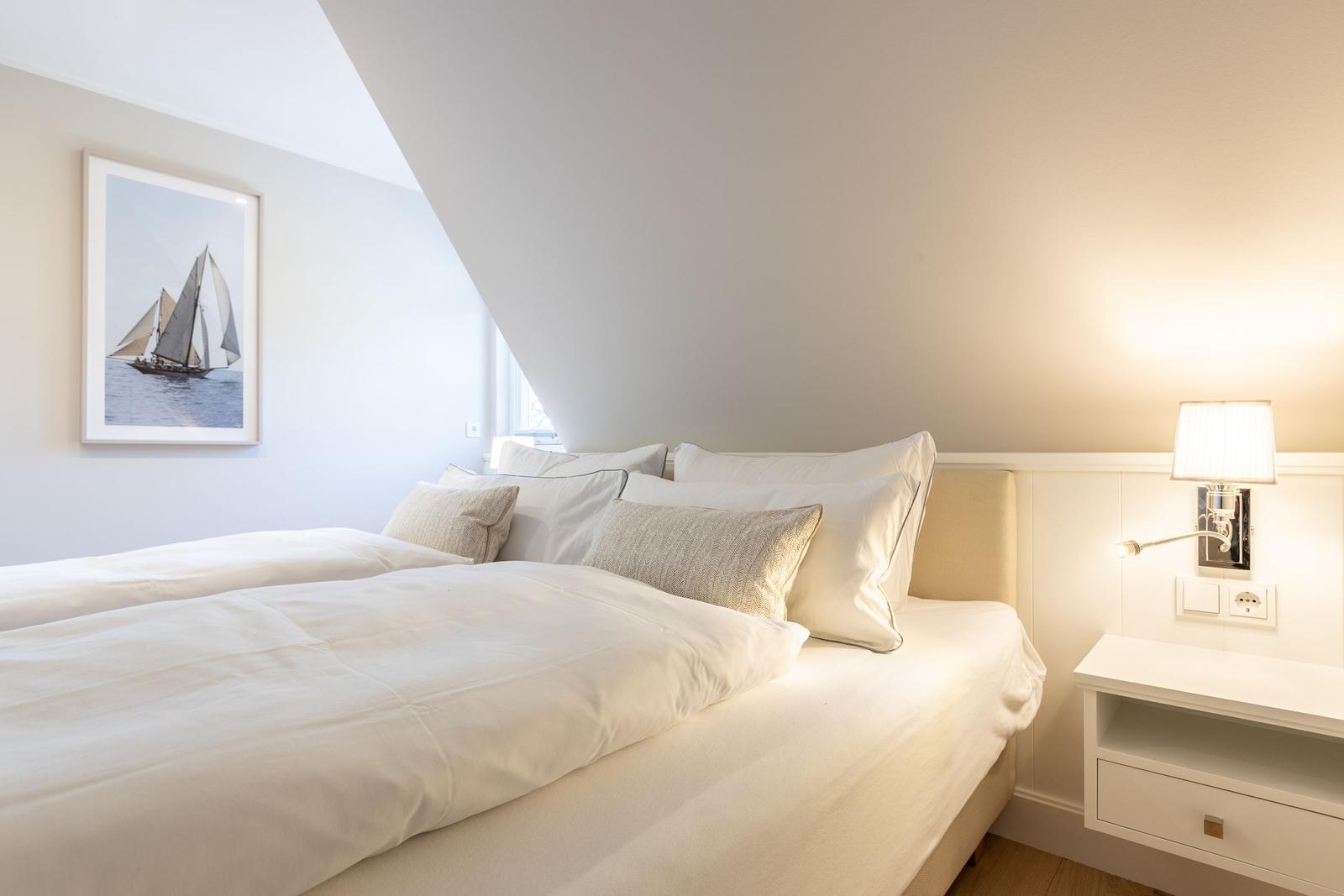 Schlafzimmer mit Bett, Nachttisch und Wandbild mit Segelboot.