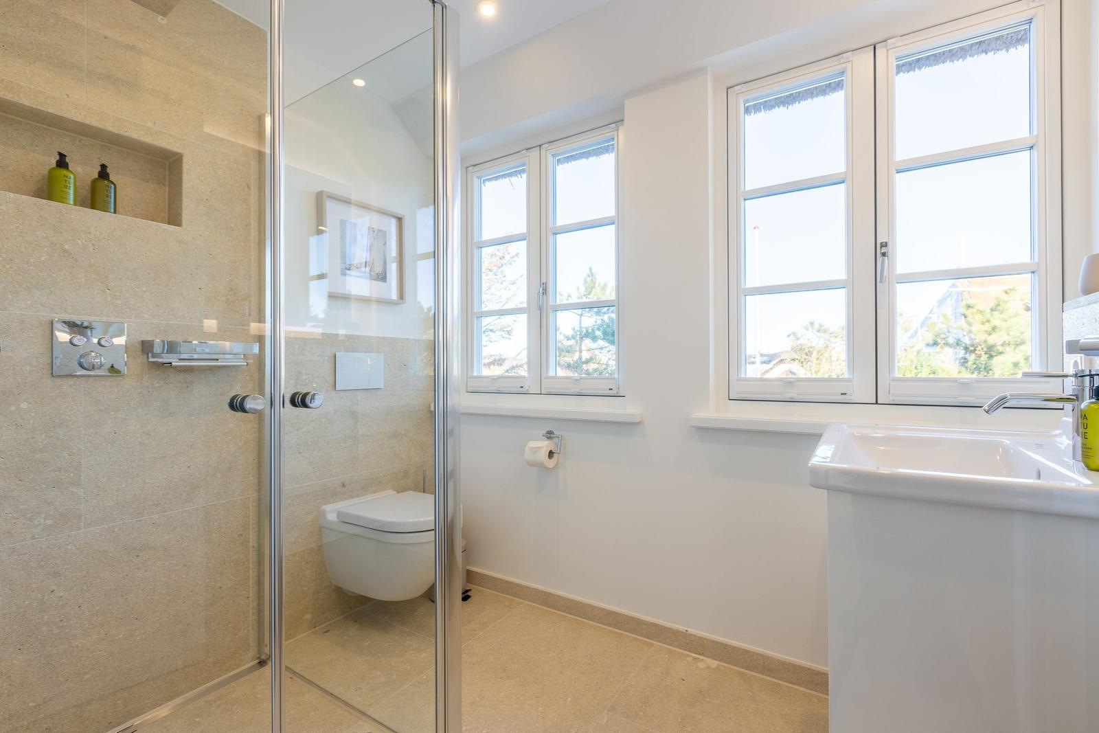 Badezimmer mit Dusche, Toilette und Waschbecken. Fenster mit Blick nach draußen.