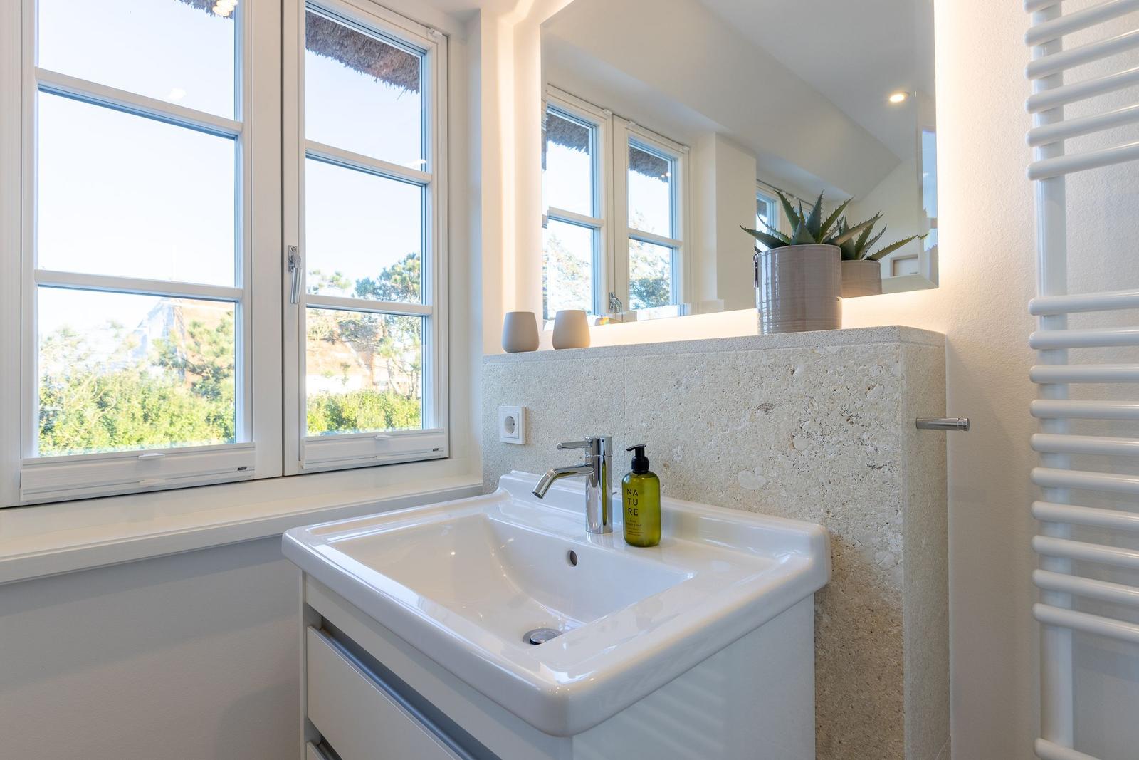 Badezimmer mit Waschbecken, Spiegel und Fenster zur Aussicht.