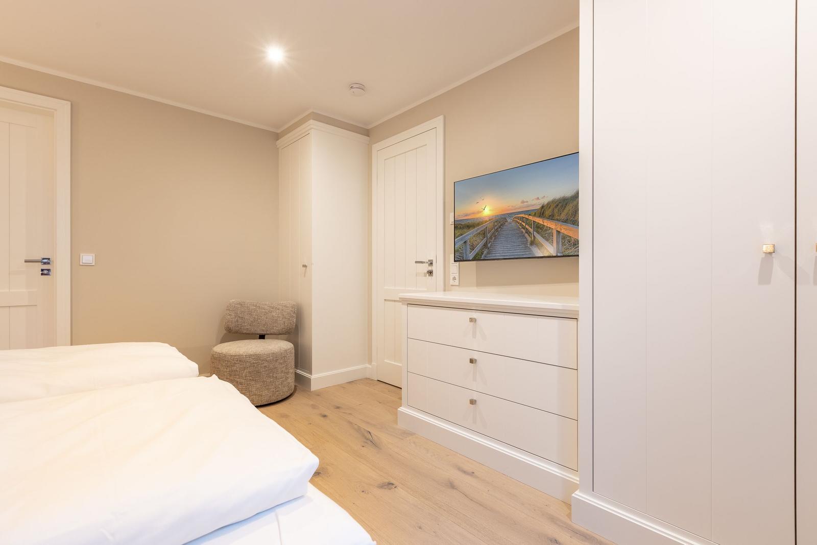 Schlafzimmer mit Bett, Kleiderschrank und Fernseher an der Wand.
