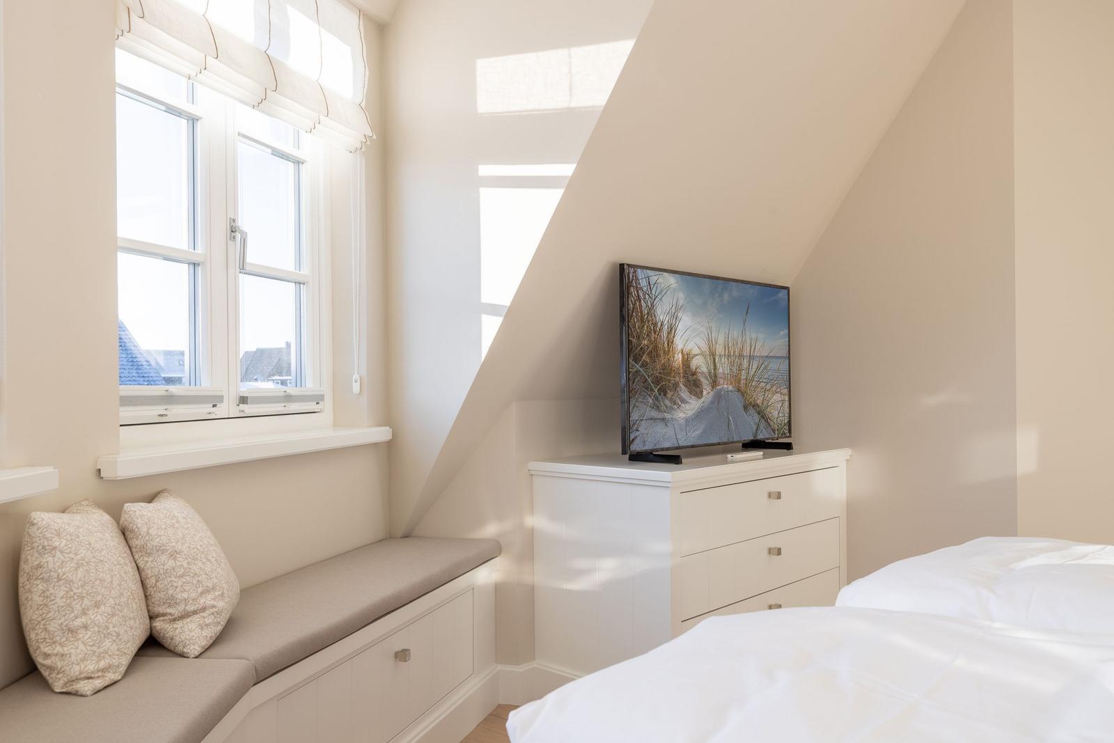 Schlafzimmer mit Fensterbank, TV und Bett unter Dachschrägen.