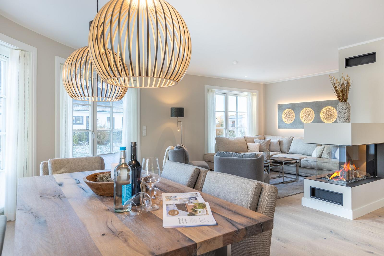 Essbereich mit Holztisch und Sitzgelegenheiten. Im Hintergrund Wohnzimmer mit Sofa und Kamin.