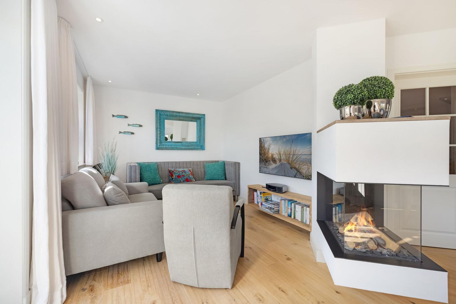Wohnzimmer mit Sofa, Sessel, Kamin und Fernseher.