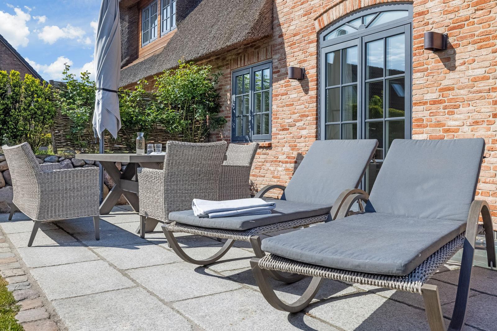 Terrasse mit Liegen, Tisch und Stühlen vor Backsteinhaus mit Dachziegeln.