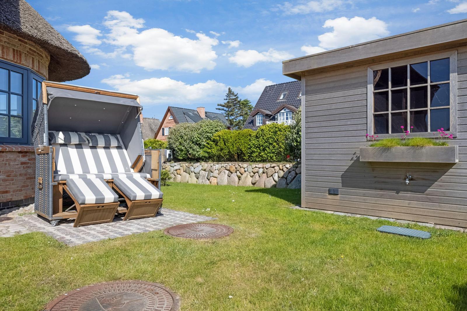 Garten mit Strandkorb, Holzhaus und Blumenkasten unter blauem Himmel.