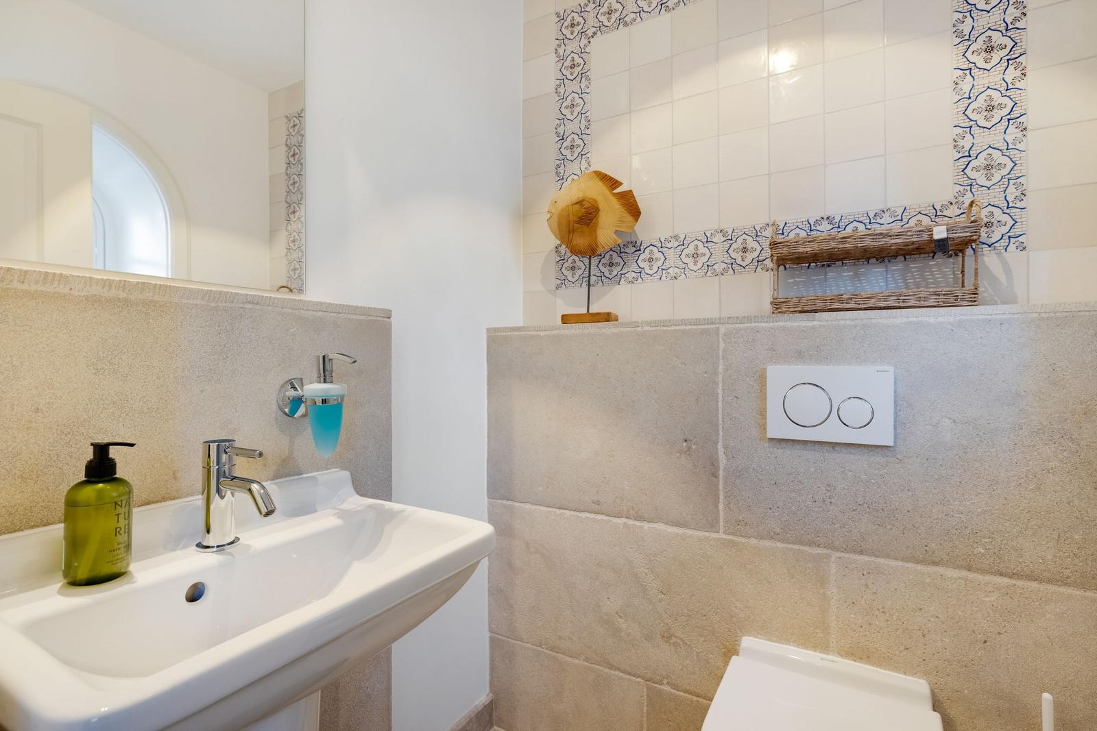 Badezimmer mit Waschbecken, Spiegel und Toilette. Wandfliesen mit blau-weißem Muster.