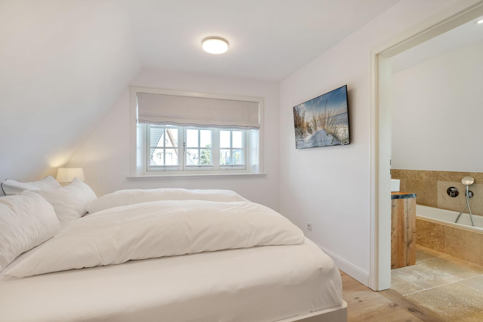 Schlafzimmer mit Doppelbett, Fenster und Bad im Anschluss.