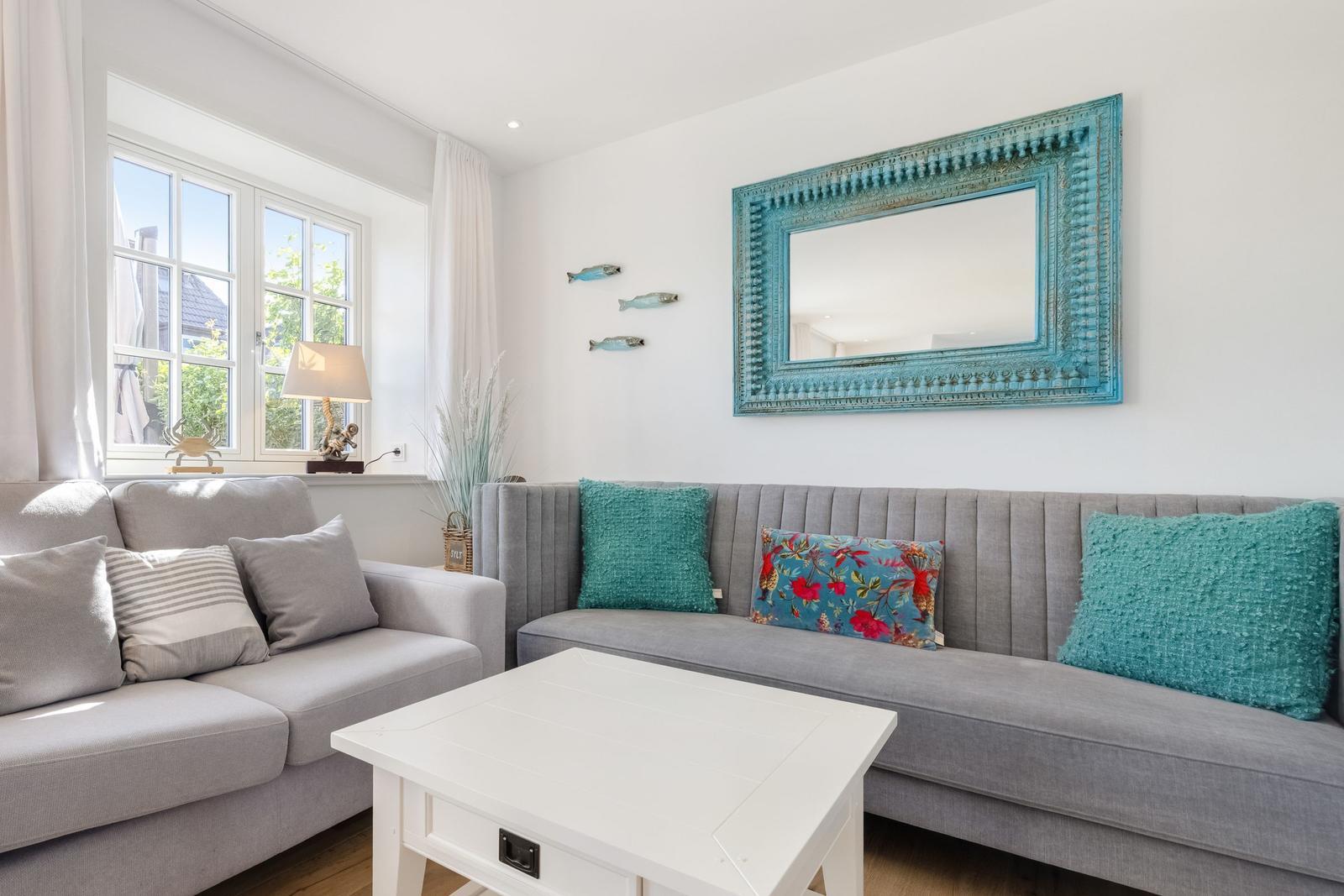 Ein Wohnzimmer mit grauem Sofa, blauem Spiegel und Fensterblick.