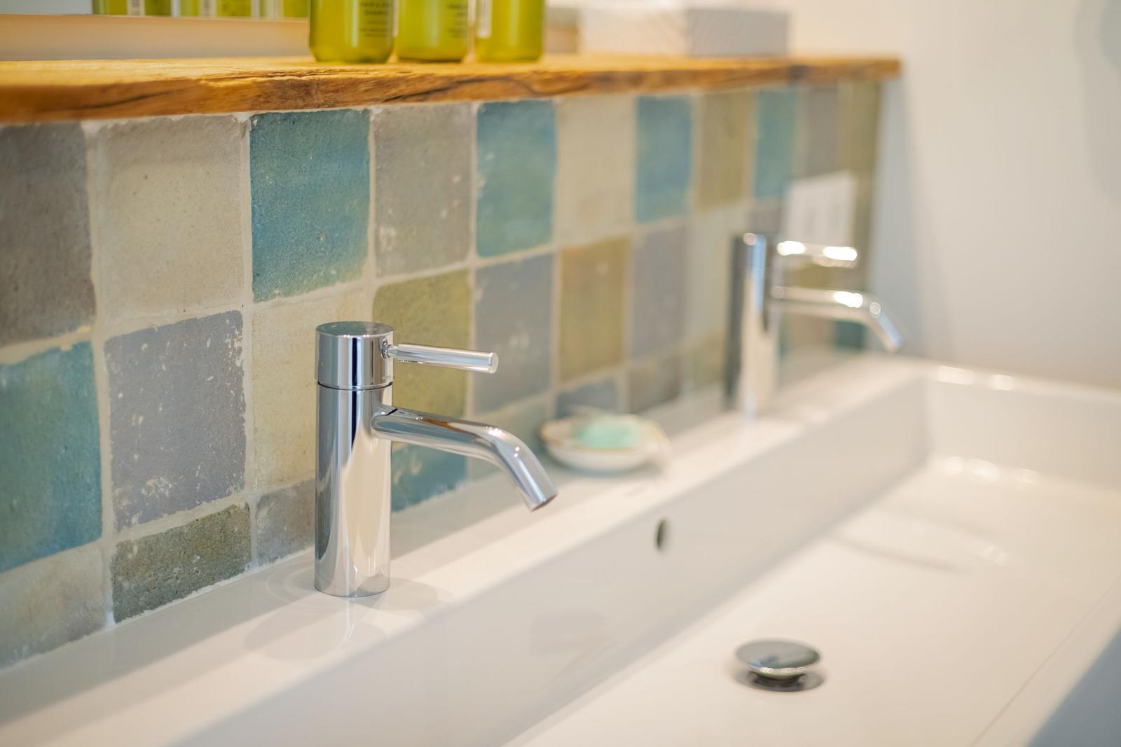 Waschbecken mit Chromarmatur und farbigen Fliesenwand.