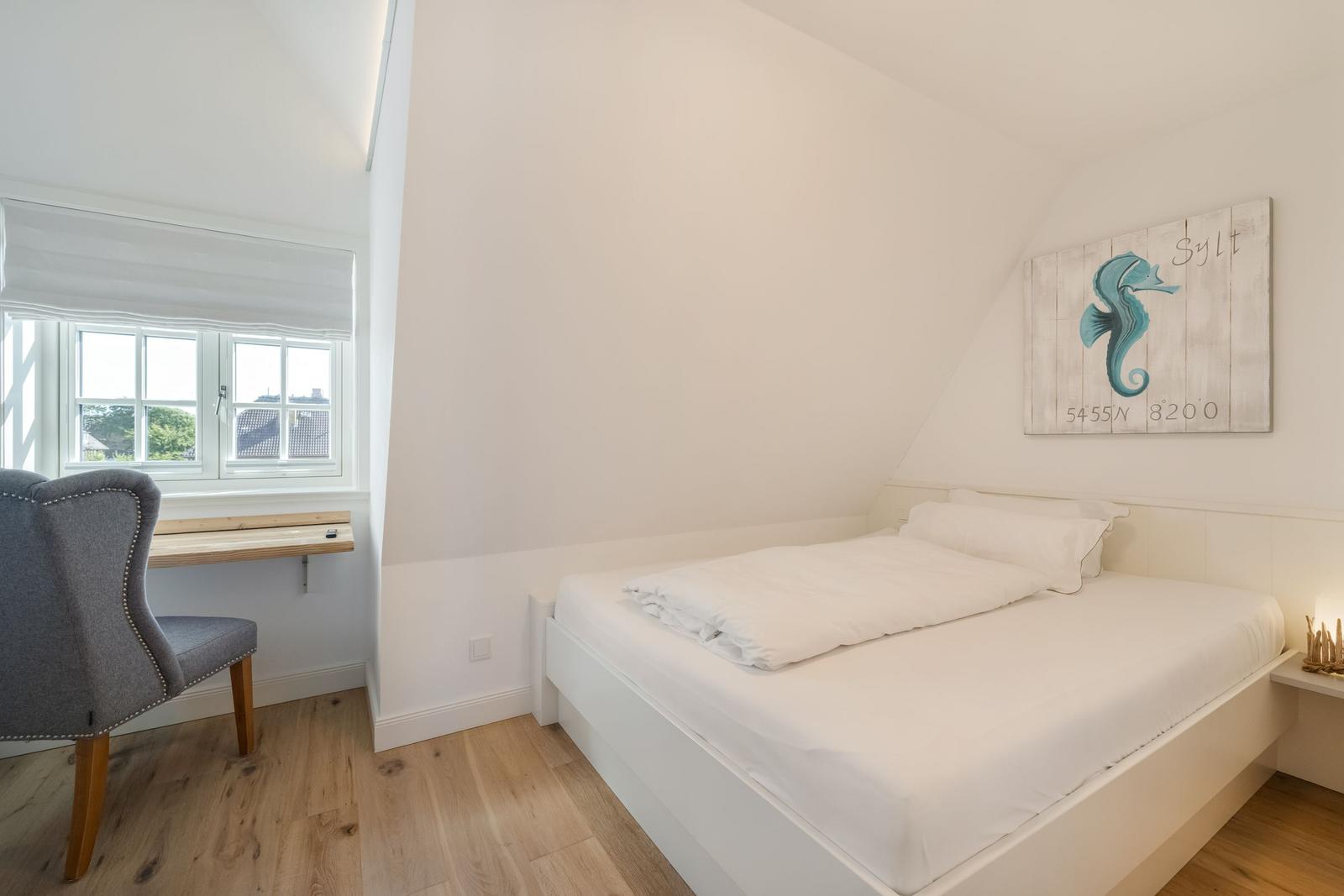 Schlafzimmer mit Bett, Schreibtisch und Wandbild mit Seepferdchen.