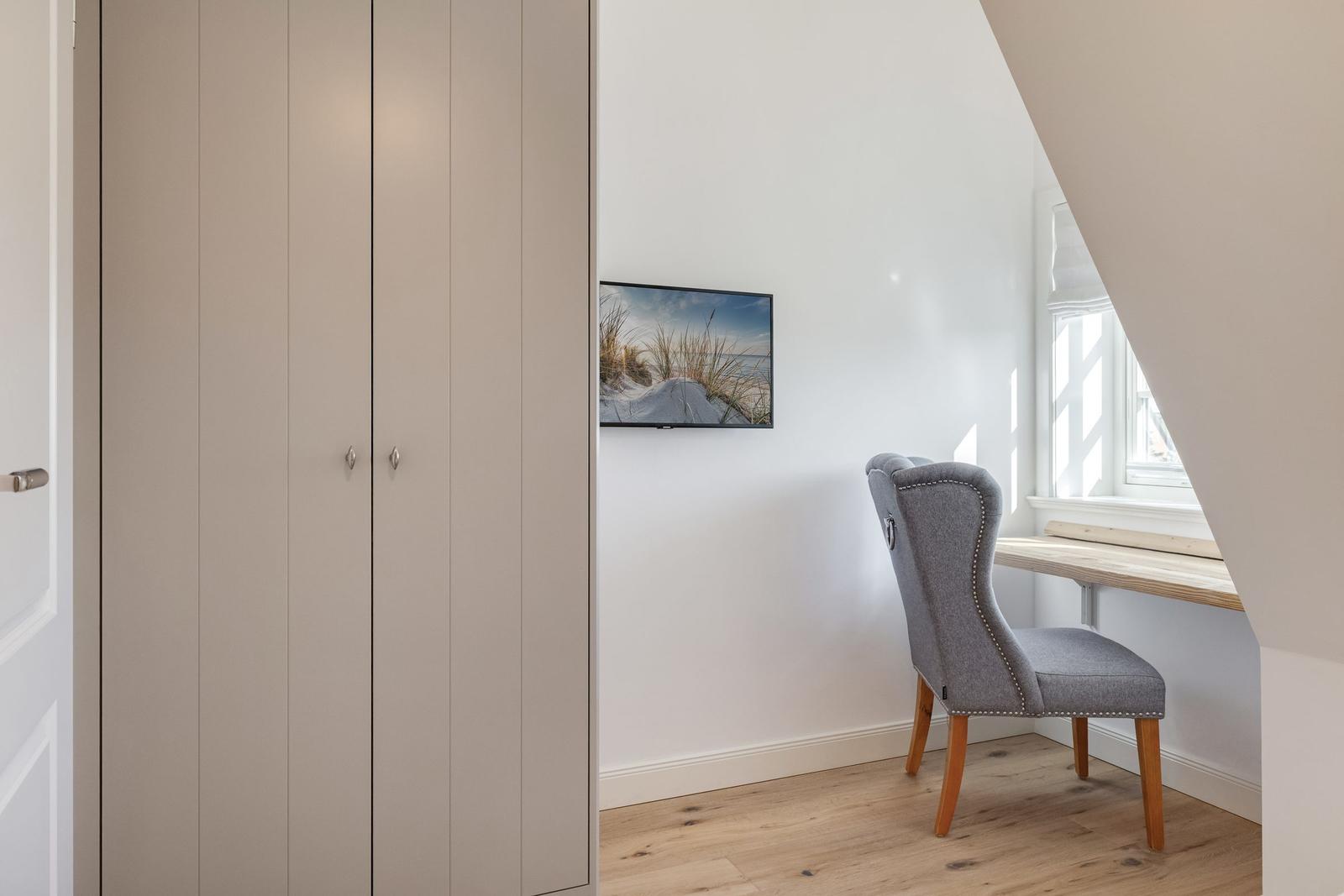 Schreibtisch mit Stuhl unter Fenster, Wandbild und Kleiderschrank im Raum.