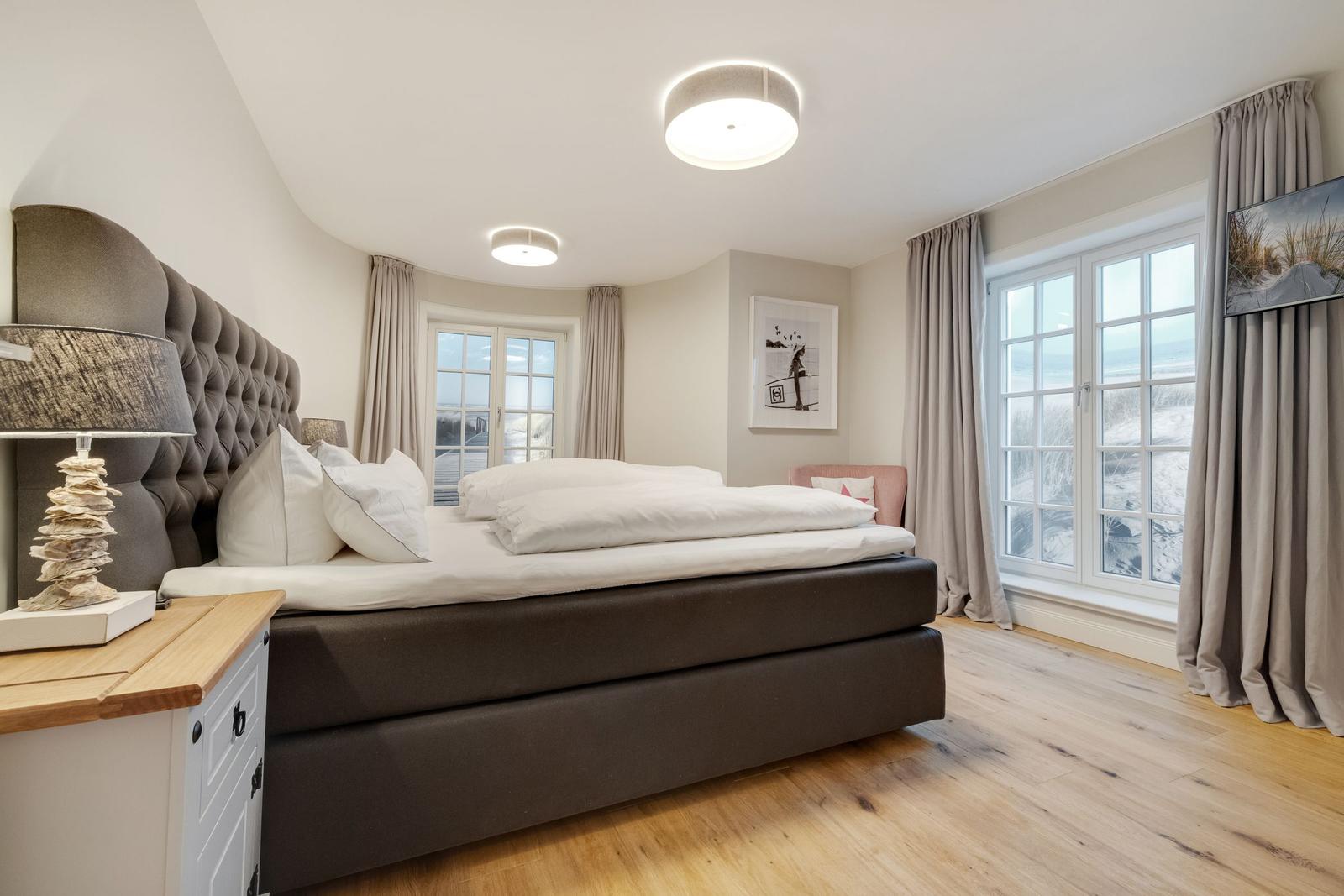 Schlafzimmer mit großem Bett, Holzboden und Fenstern mit Meerblick.