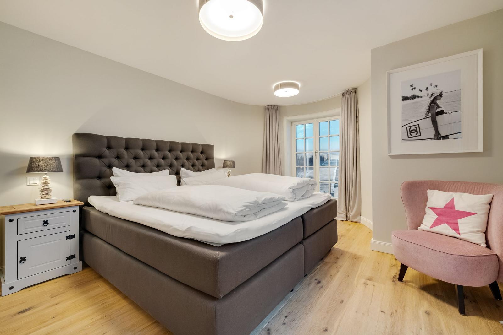 Schlafzimmer mit Bett, Nachttisch und Sessel. Fenster mit Blick nach draußen.