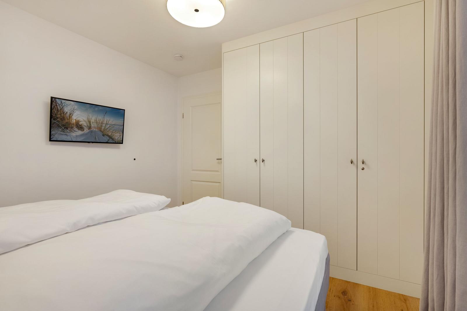 Schlafzimmer mit weißem Bett, Kleiderschrank und Wandbild