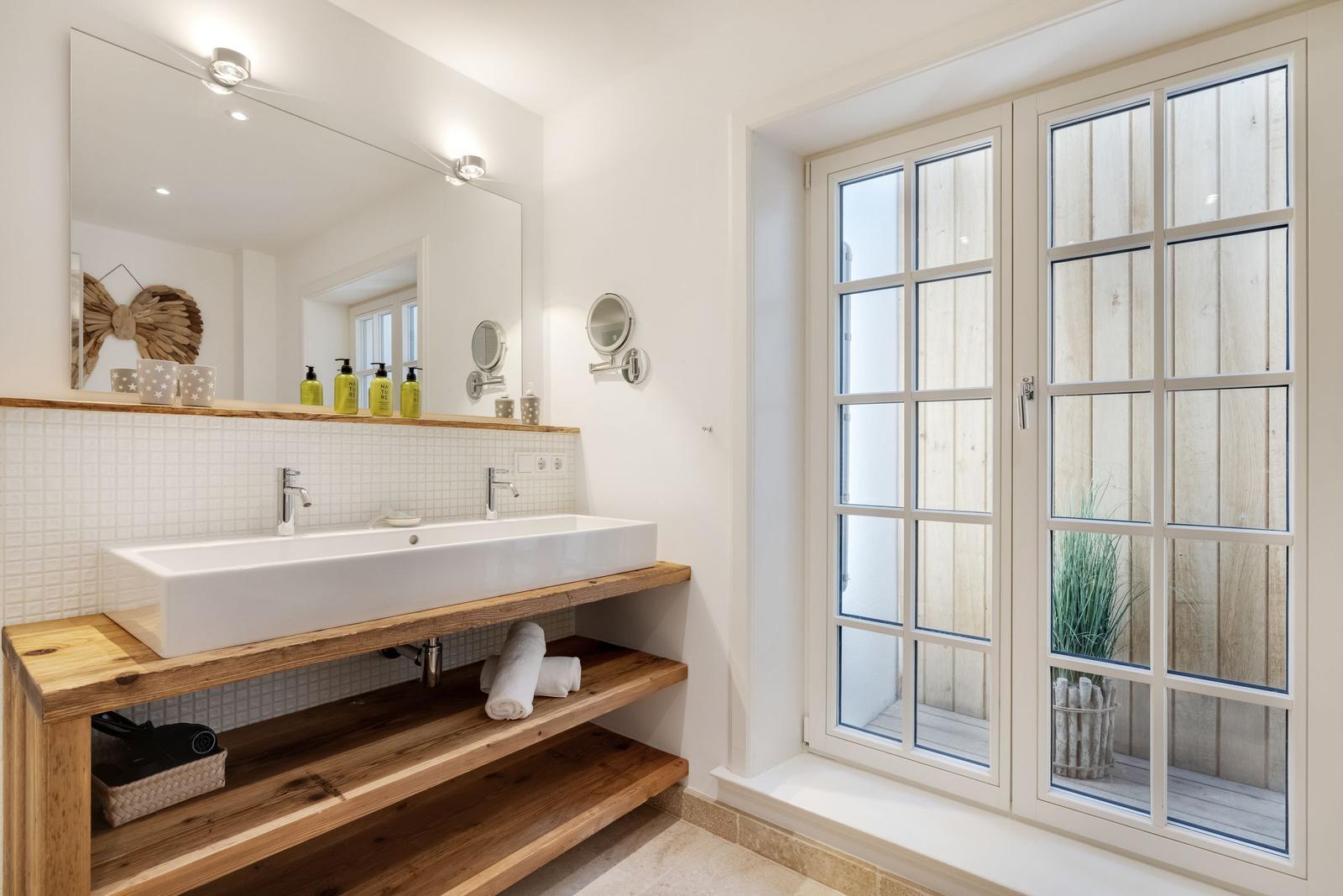 Badezimmer mit Holzwaschtisch, Spiegel und französischem Fenster.