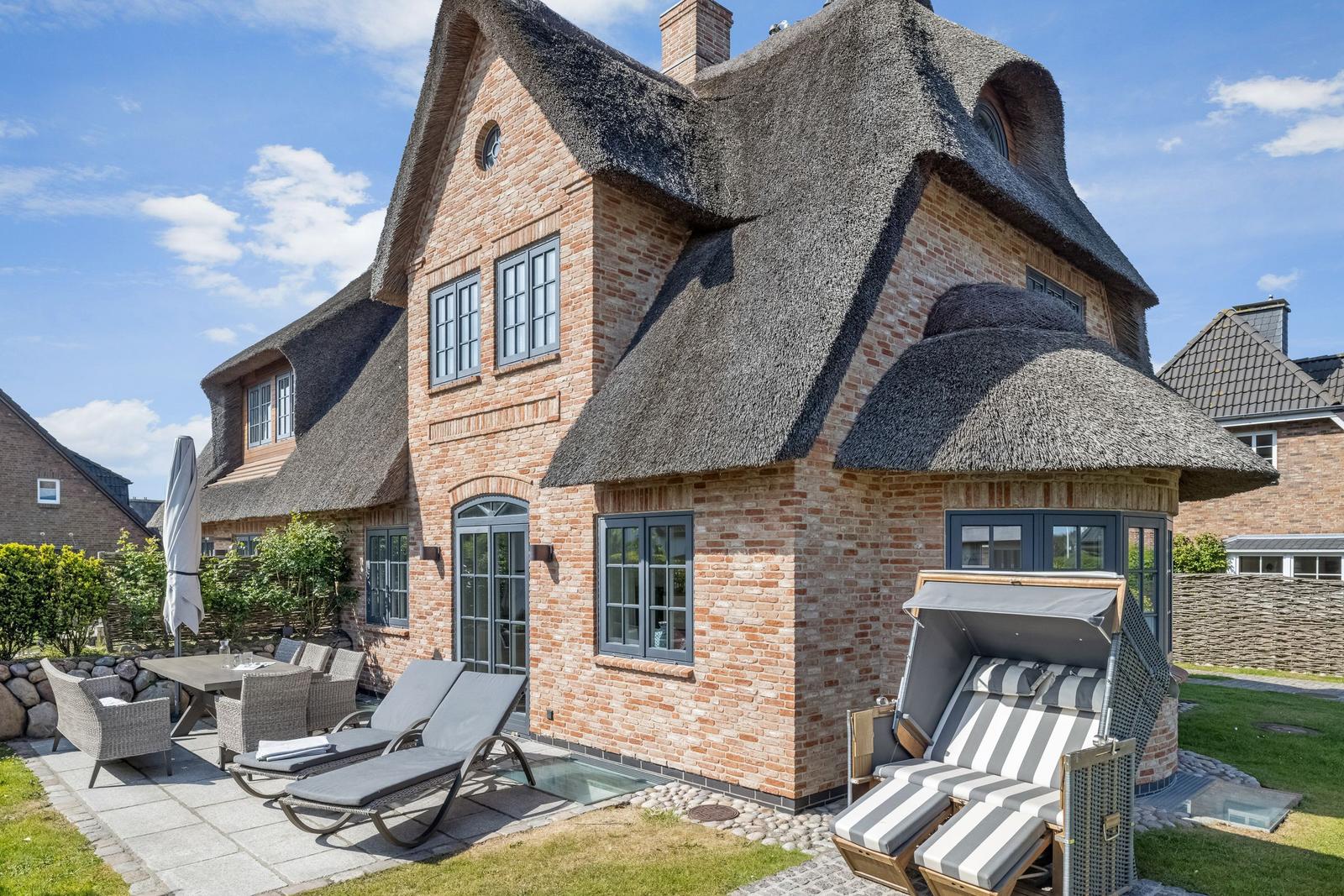 Haus mit Strohdach, Terrasse und Liegestühle im Garten.