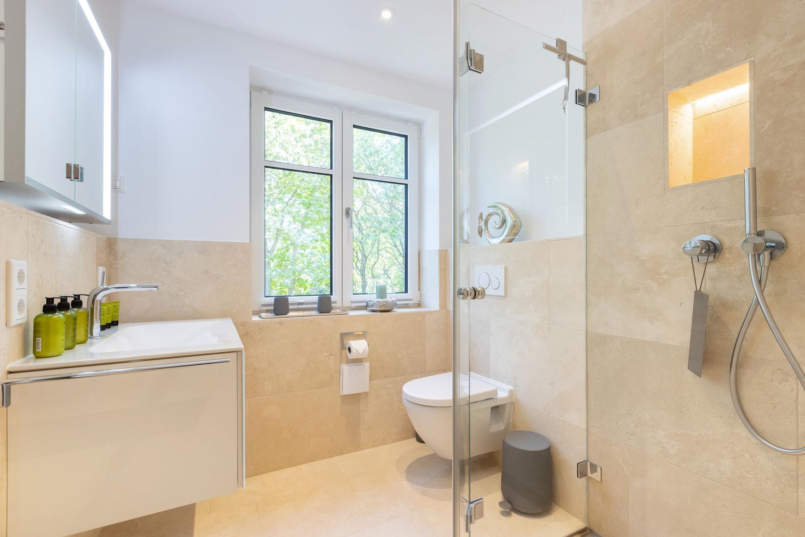 Badezimmer mit Dusche, Waschbecken und Fenster mit Blick auf Bäume.