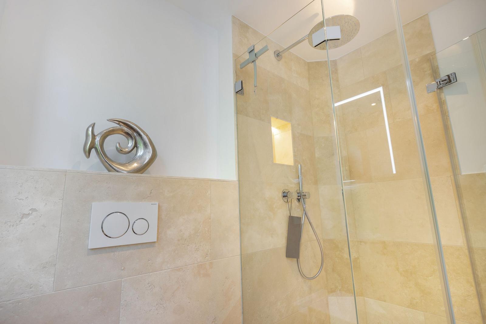 Dusche mit Glaswand und moderner Duschkopf. Wand mit Toilettensteuerung und Skulptur.
