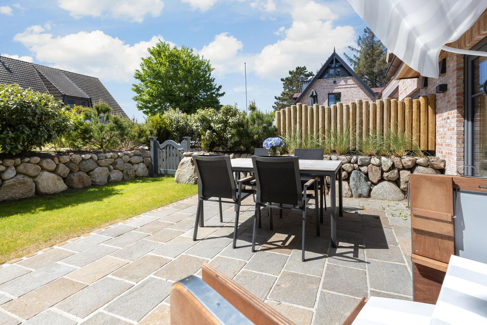 Terrasse mit Tisch, Stühlen und Steinpflaster. Hinterhof mit Holzzaun und Grünflächen.