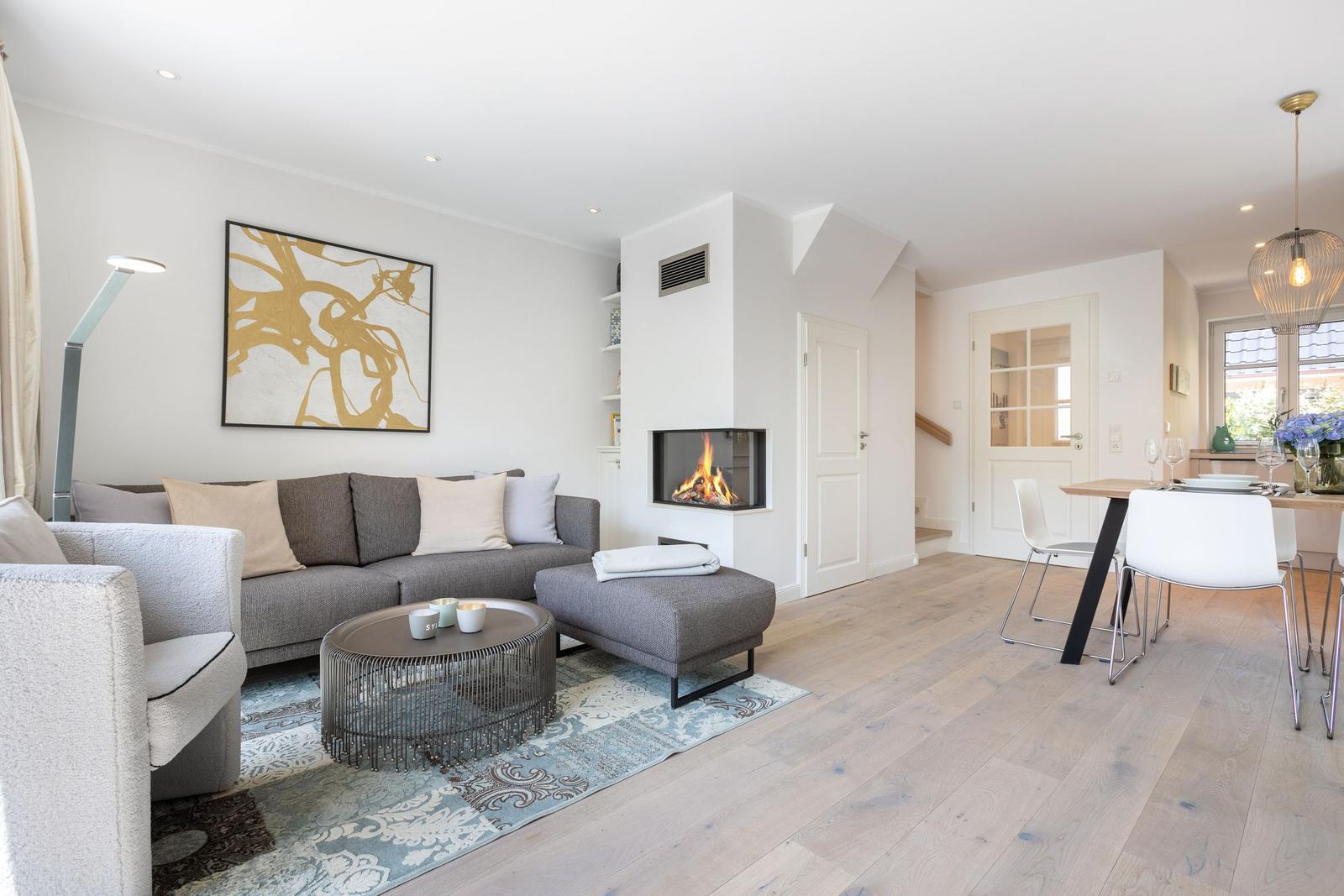 Wohnzimmer mit Sofa, Kamin und Esstisch. Holzboden und Wandbild sichtbar.