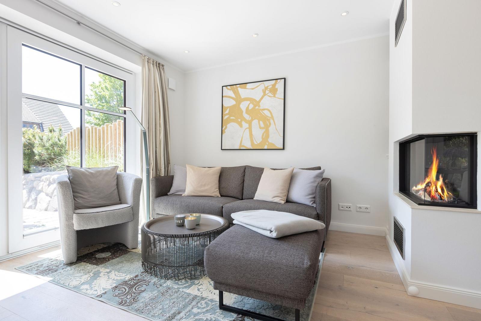 Wohnzimmer mit Sofa, Sessel, Kamin und großem Fenster.