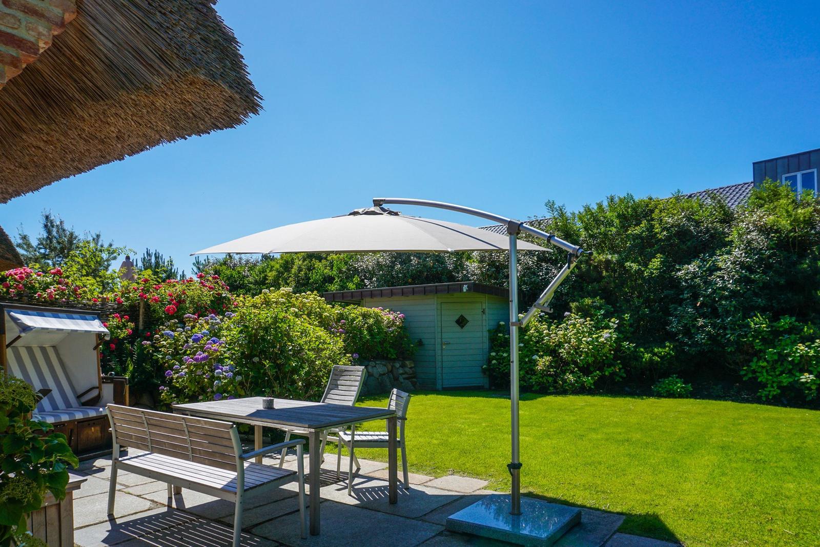 Garden with table, chairs, and umbrella. Lawn and flower beds.