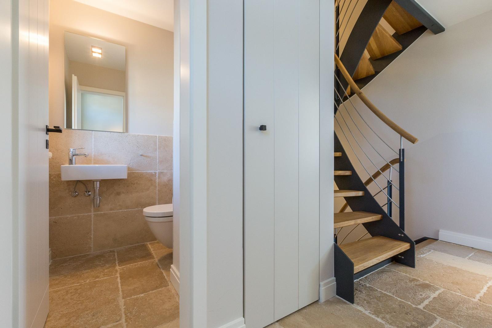 Bathroom with sink and toilet next to a spiral staircase.