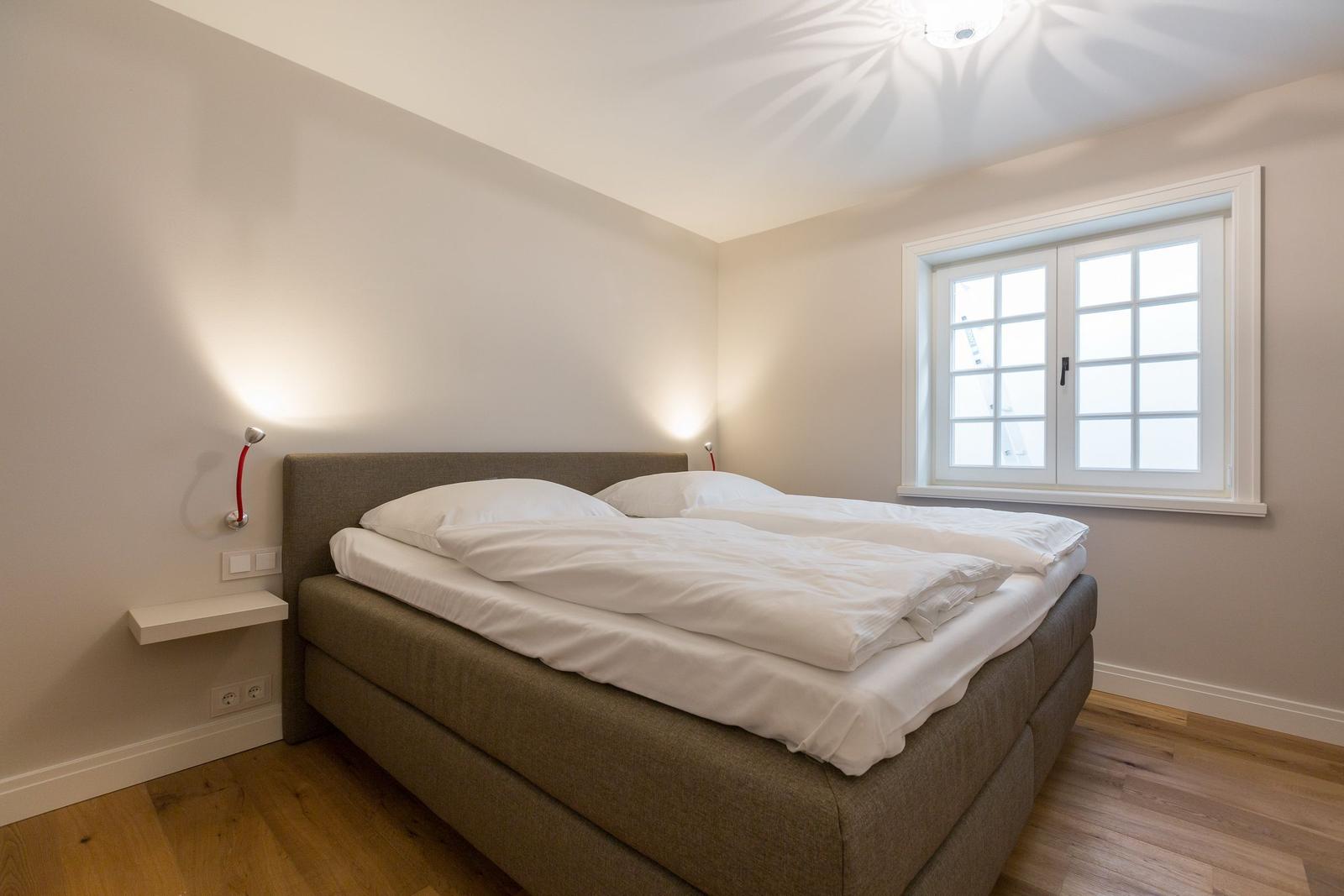 Bedroom with double bed, window, and wall lamp.