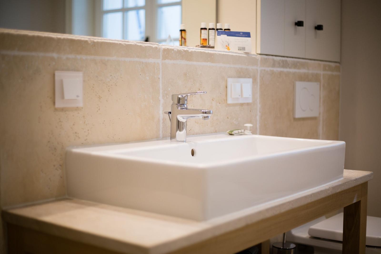 Sink on wooden vanity with stone wall and faucet