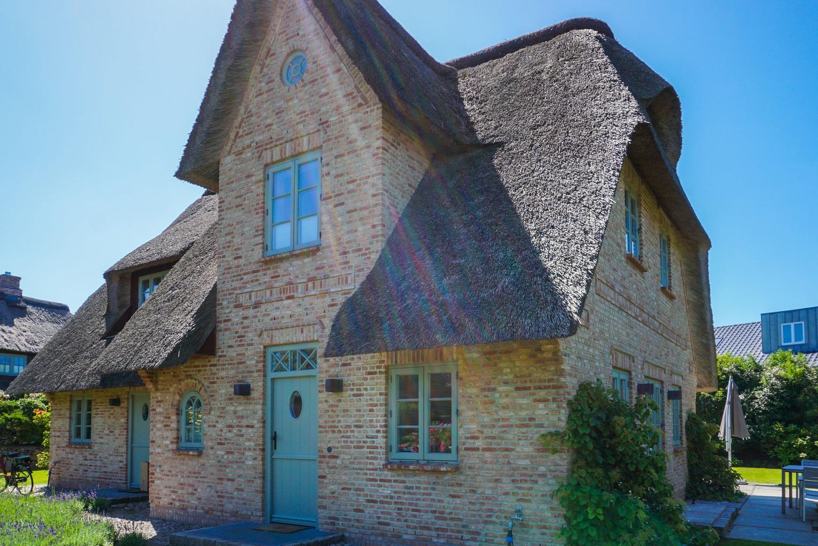 A house with thatched roof and brick facade. Door and windows are light blue.