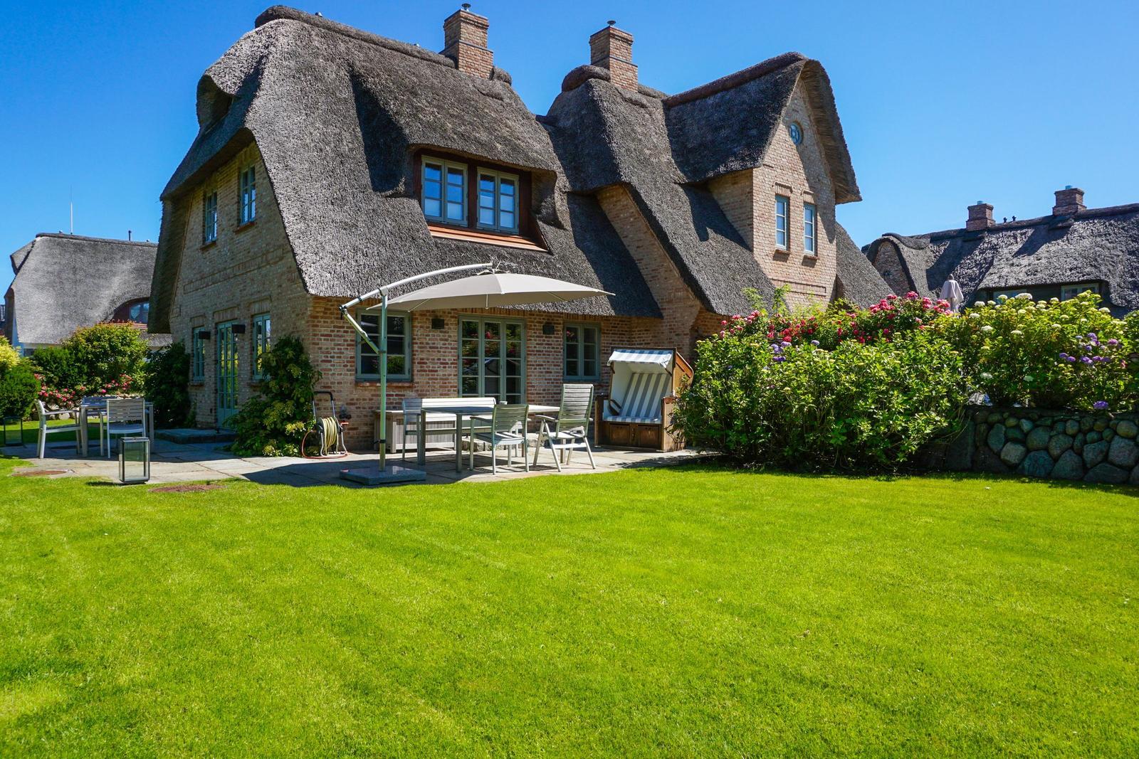 House with thatched roof, garden with seating and flower beds.