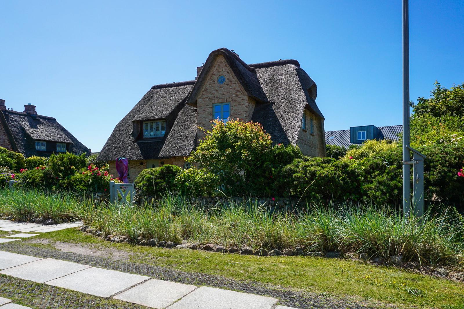 Cottage with thatched roof, green garden and stone path.