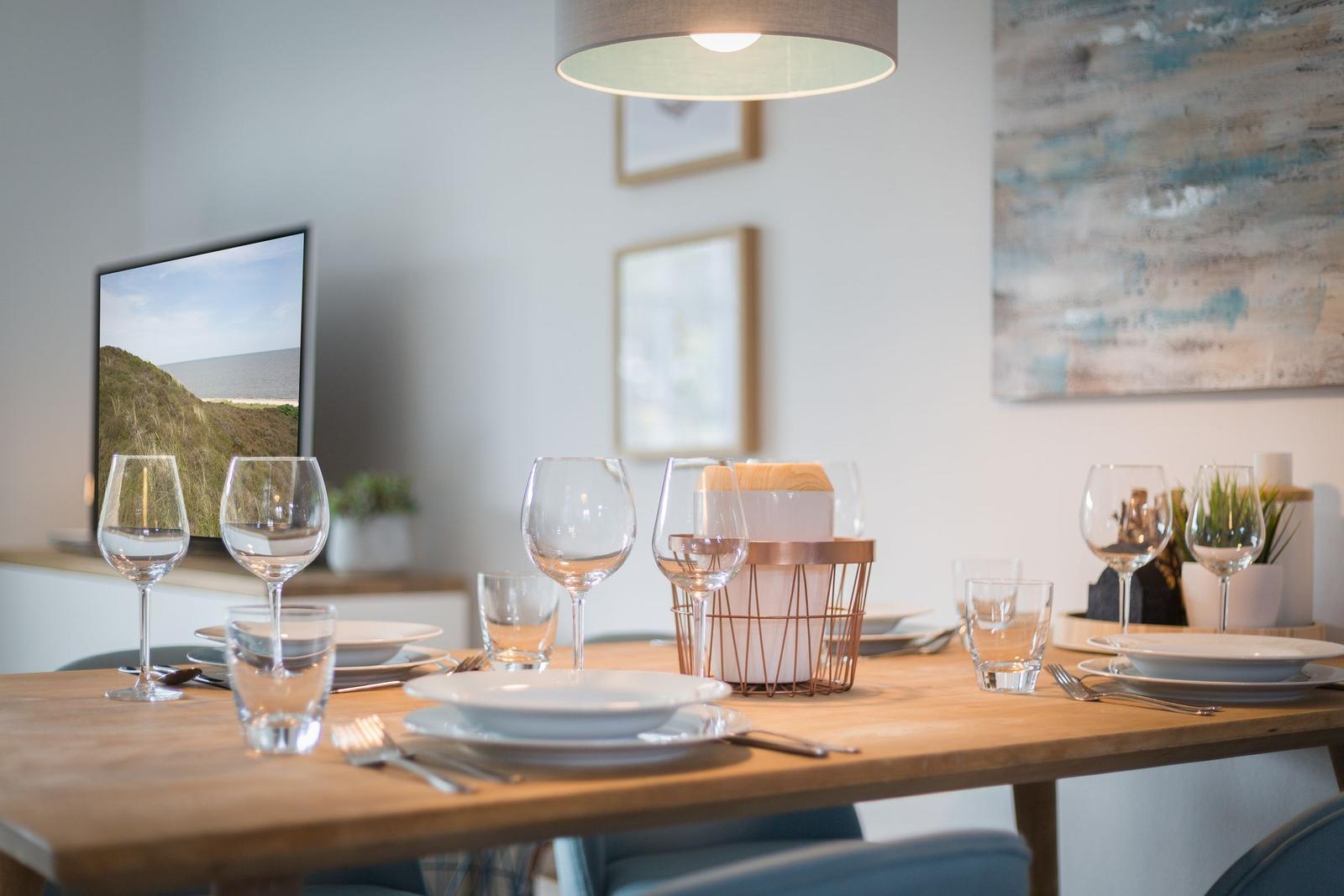 Esstisch mit Geschirr und Gläsern, Wandbild und TV im Hintergrund.
