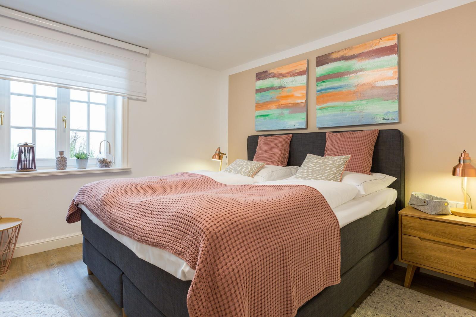 Schlafzimmer mit Bett, zwei Nachttischen und Wandbildern.