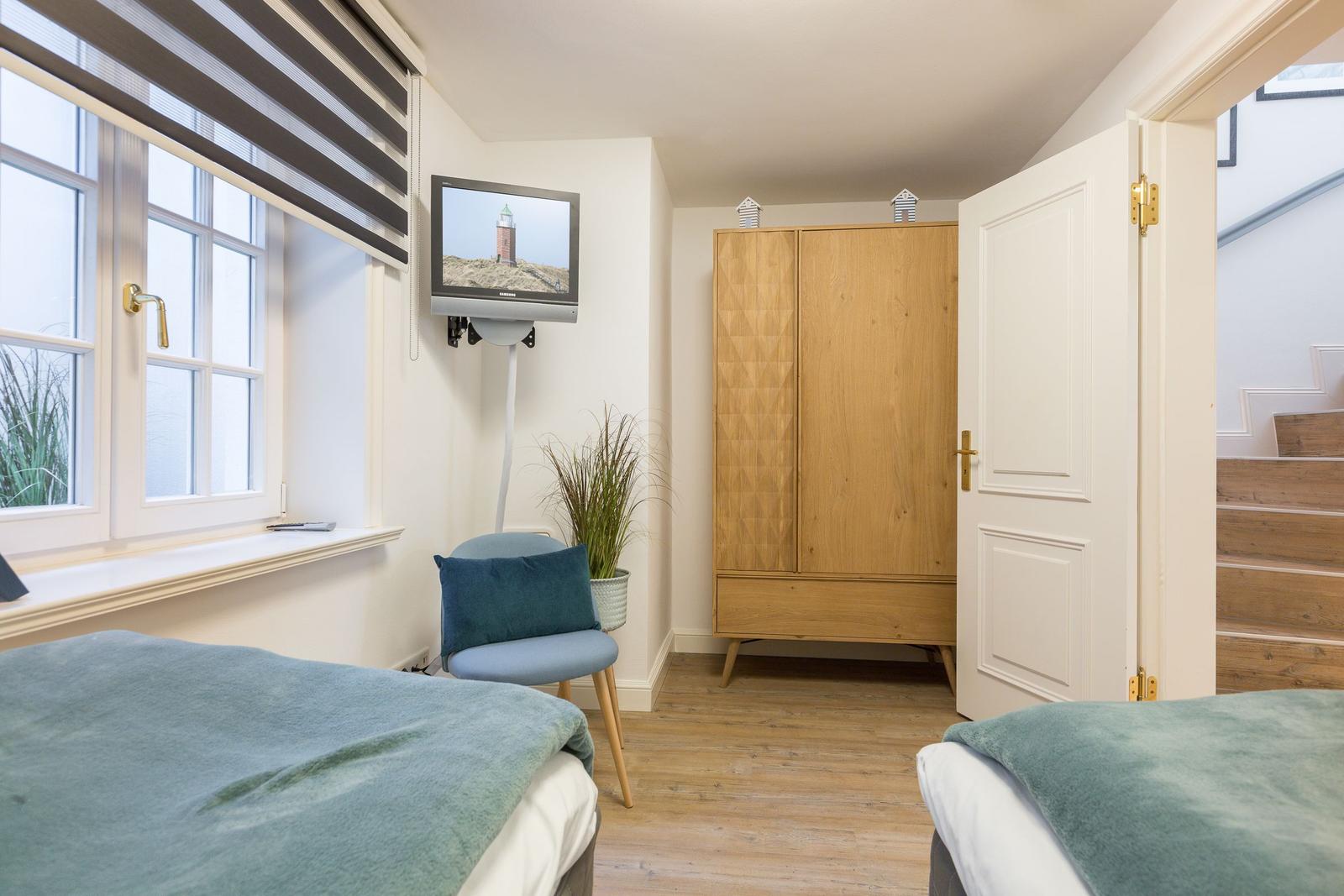 Zwei Betten, Kleiderschrank, TV und Fenster mit Jalousie.